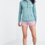 Stitch Fix model wearing women's golf attire outfit including white visor, blue quarter-zip, pink shorts and sneakers.