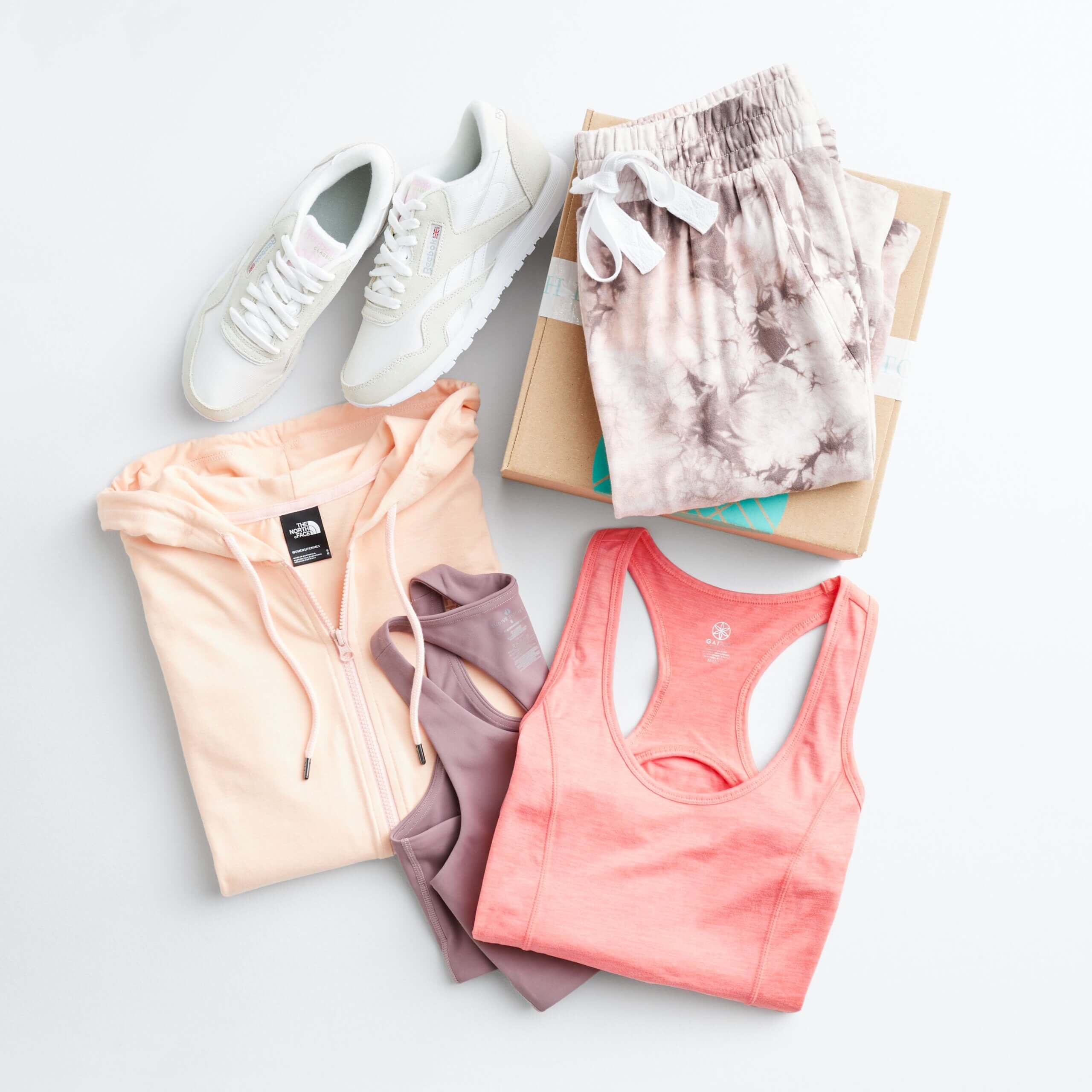 Stitch Fix women’s hiking outfit with sports bra, pink tank, zip-up hoodie, sneakers next to printed joggers on top of Fix box.