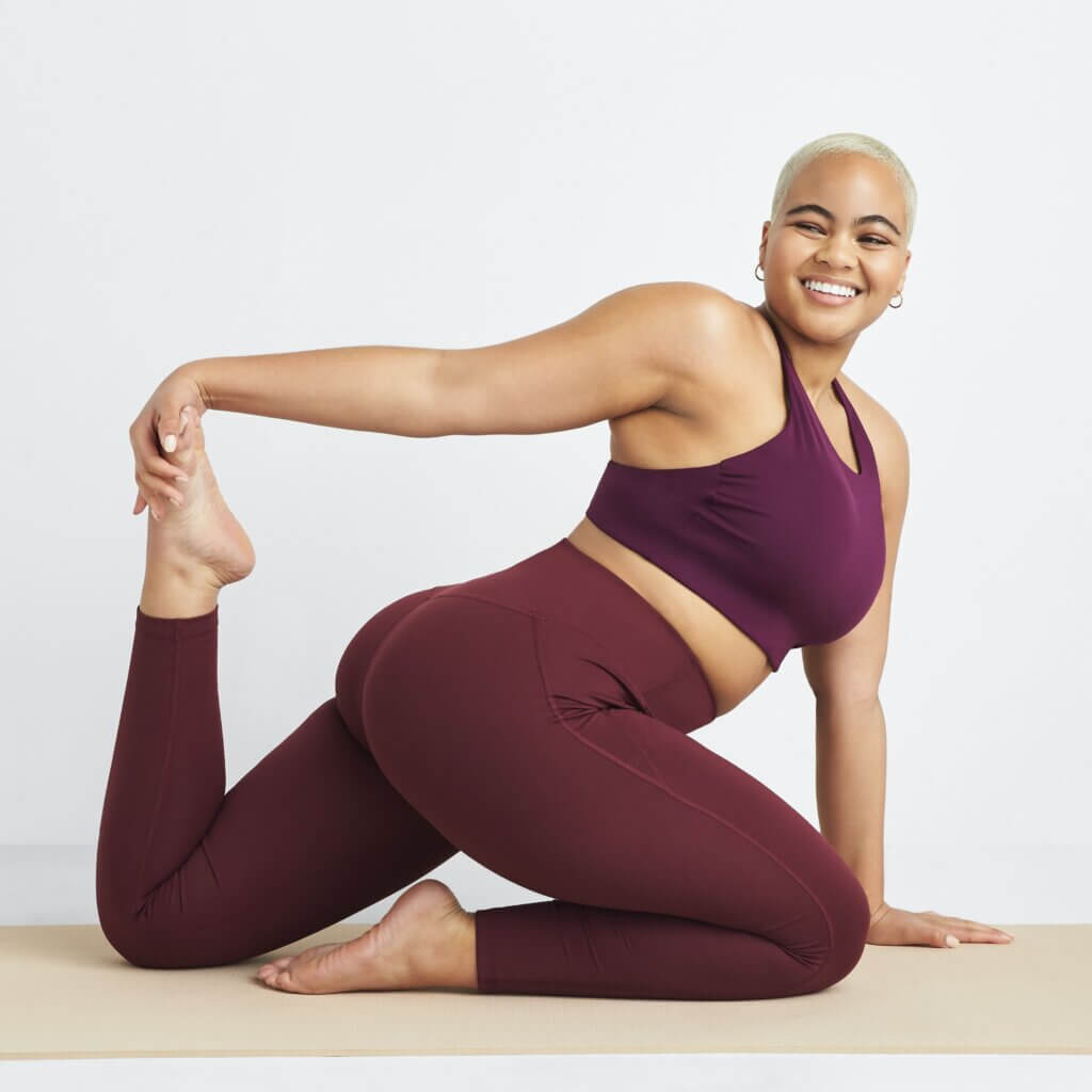Stitch Fix women's model in stretch pose wearing a yoga outfit featuring matching burgundy sports bra and leggings.