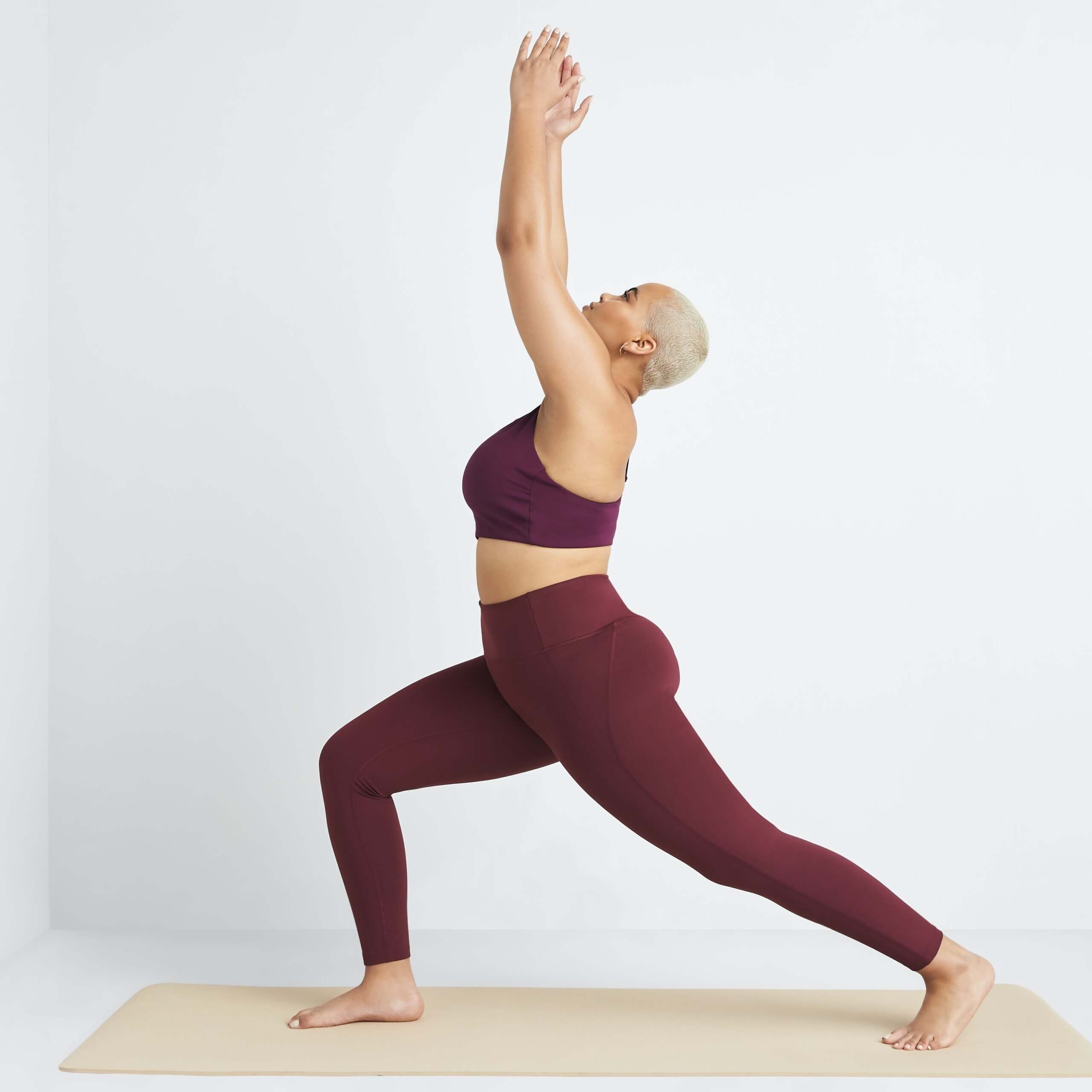Stitch Fix women's model in warrior 1 pose wearing a yoga outfit featuring matching burgundy sports bra and leggings.