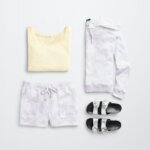 Stitch Fix women’s comfy road trip outfit with yellow tank, silver slide sandals and purple and white tie-dye hoodie and shorts set.
