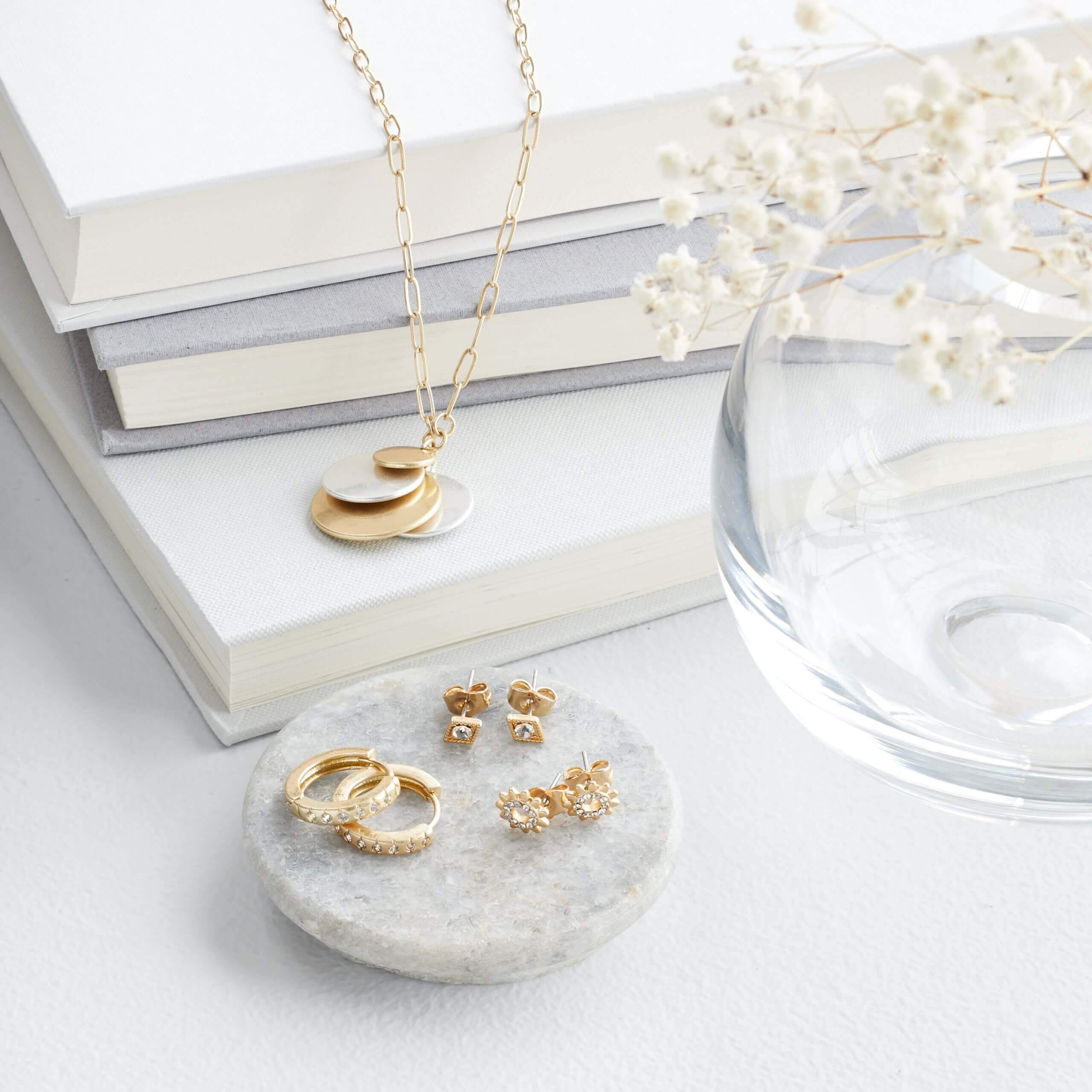 Stitch Fix women's gold and silver pendant necklace and earring set displayed with a stack of books, tray and vase with white flowers.