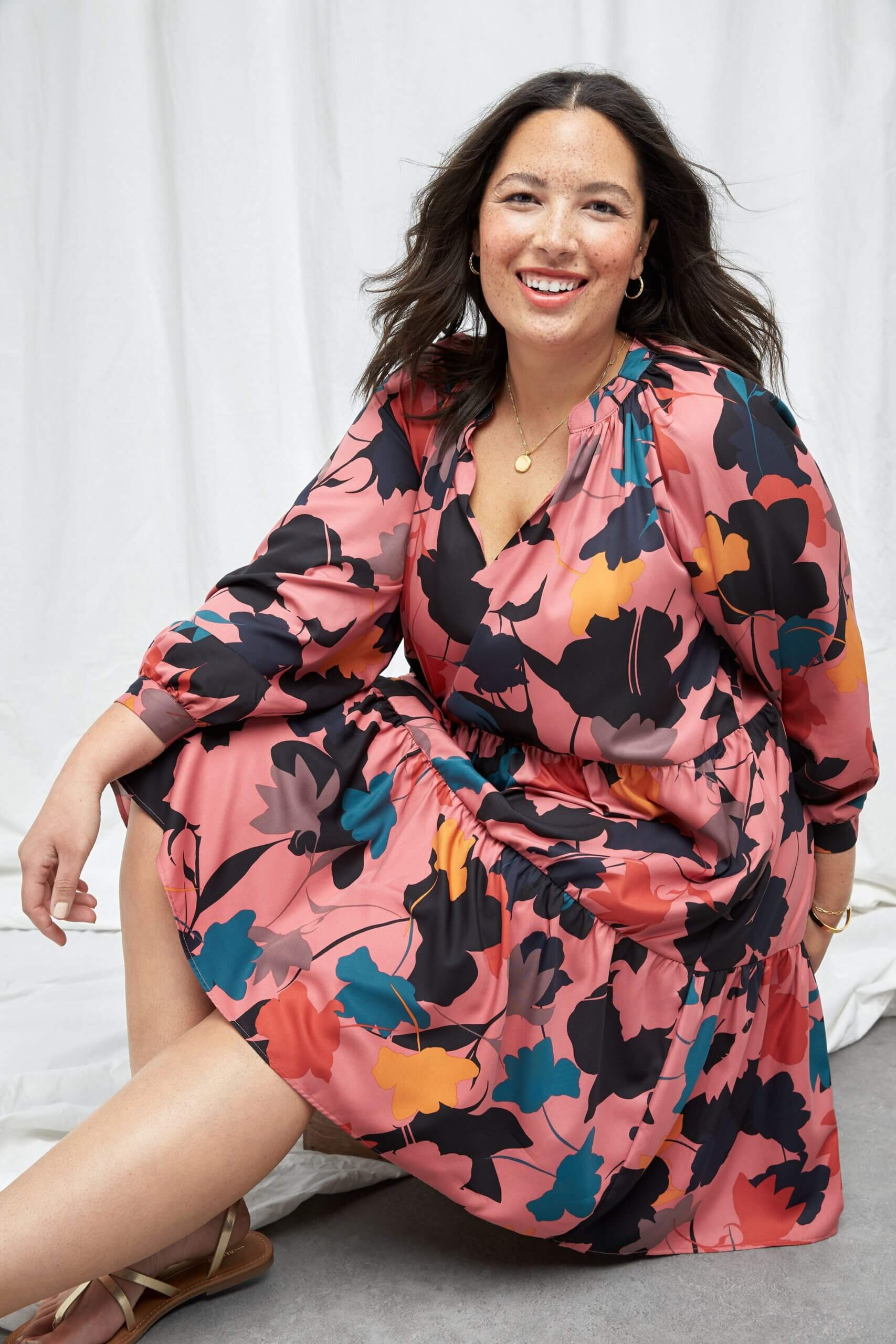 Stitch Fix model wearing spring 2022 fashion with pink abstract print dress, gold sandals, pendant necklace and hoop earrings.