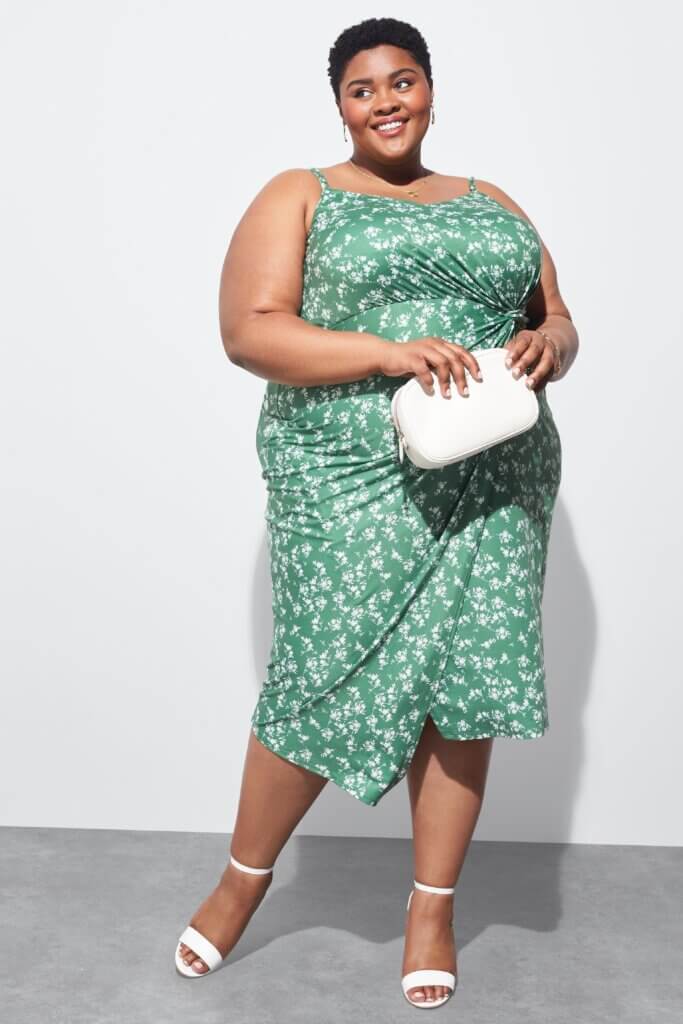 Stitch Fix model wearing women's semi-formal wedding attire featuring green printed dress, white heels and clutch.
