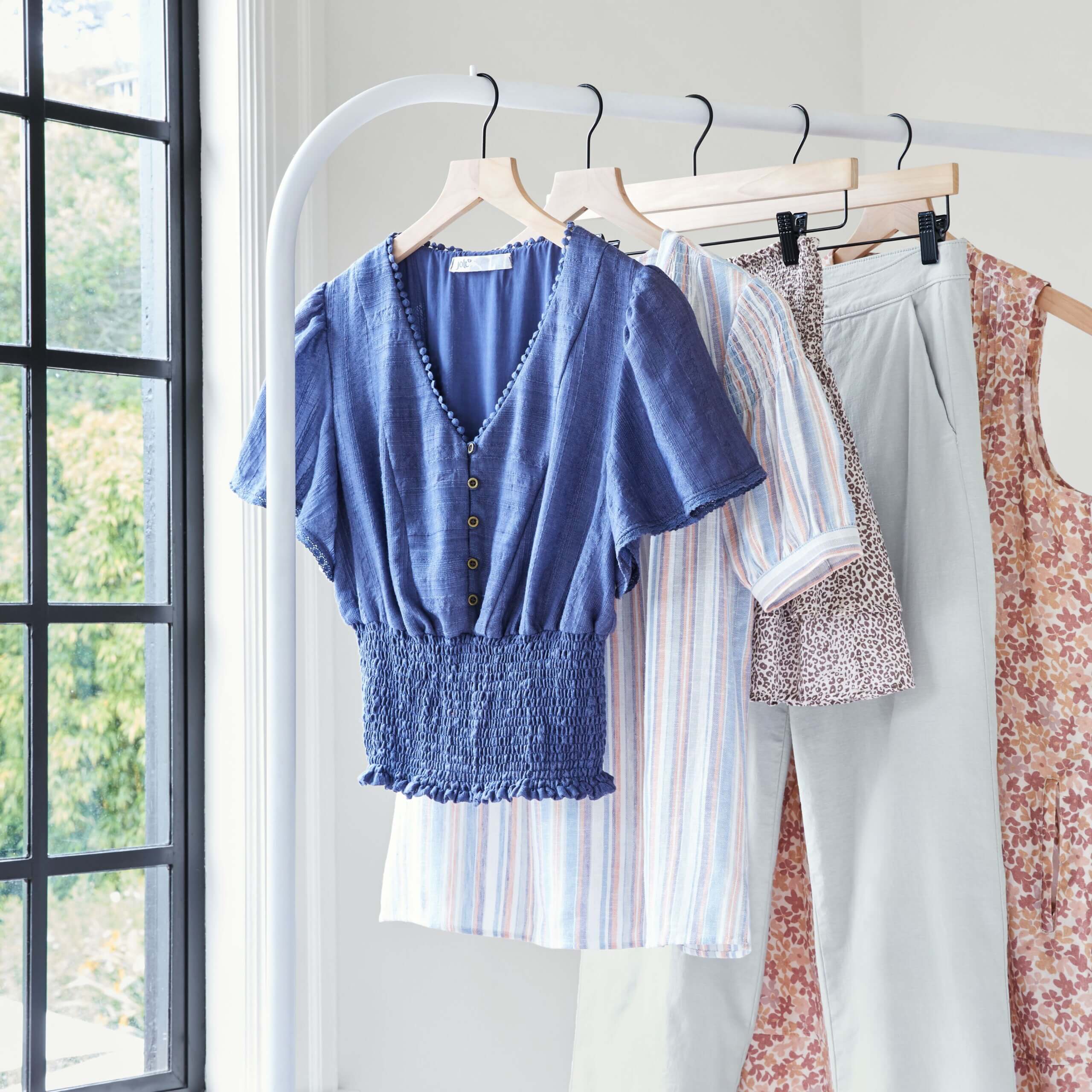 Stitch Fix women’s coastal grandmother style tops, bottoms and dresses in blue, white, light pink and tan hanging on a rack.