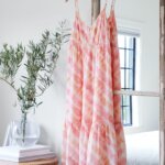 Stitch Fix women’s casual wedding beach attire with tie-dye dress hanging on mirror next to plant in vase and books on table.