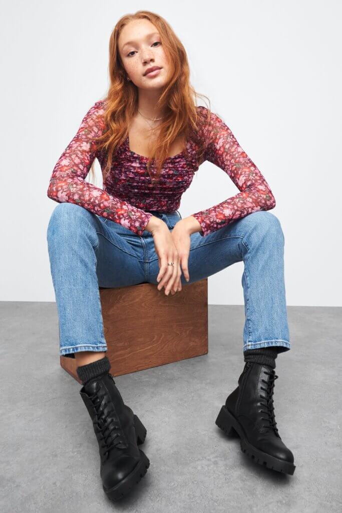 Stitch Fix model wearing women's edgy feminine style outfit with long-sleeve floral print top, blue jeans and black boots.
