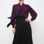 Stitch Fix model wearing women’s business formal outfit with black midi skirt and plum long-sleeved blouse with neck tie.