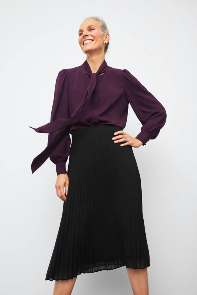 Stitch Fix model wearing women’s business formal outfit with black midi skirt and plum long-sleeved blouse with neck tie.