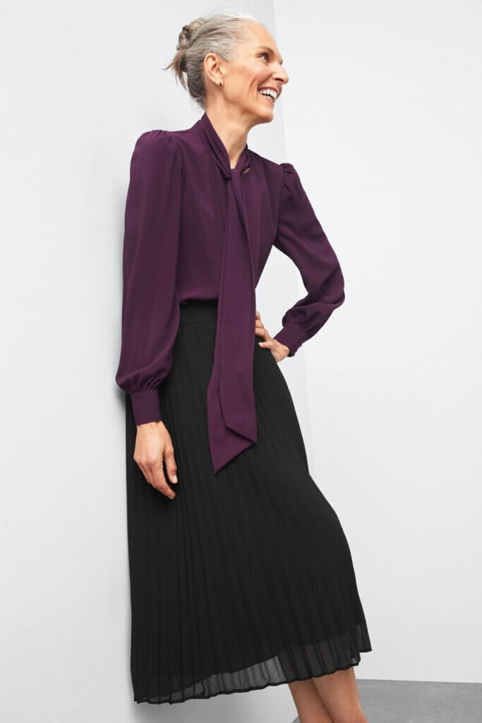 Stitch Fix model wearing women's business professional attire featuring tie neck bow blouse and pleated midi skirt.