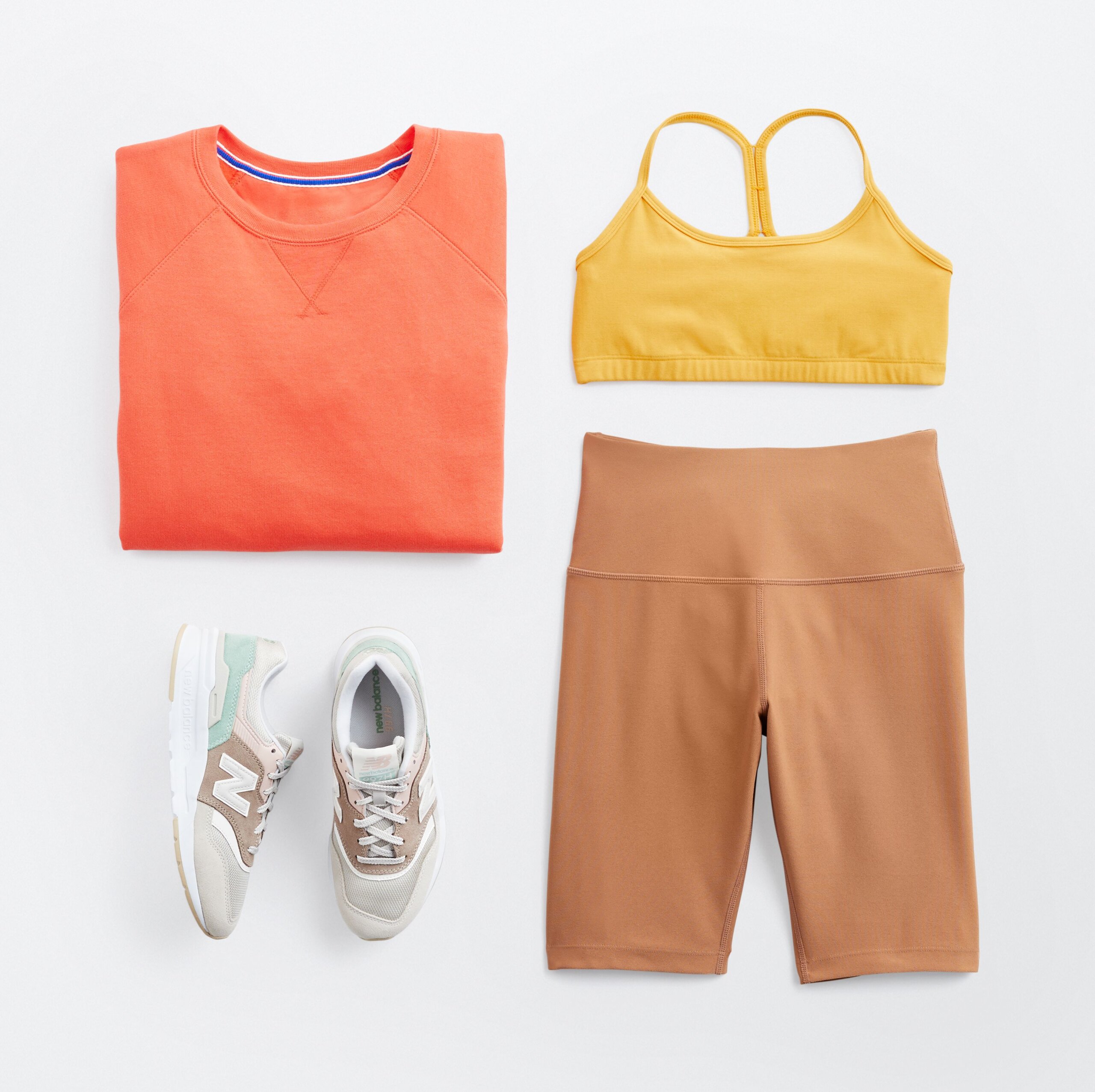 Stitch Fix women’s tennis outfit including an orange sweatshirt, yellow sports bra, tan bike shorts and white sneakers.