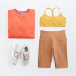 Stitch Fix women’s outfit for what to wear hiking with yellow sports bra, orange sweatshirt, camel biker shorts and fashion sneakers.