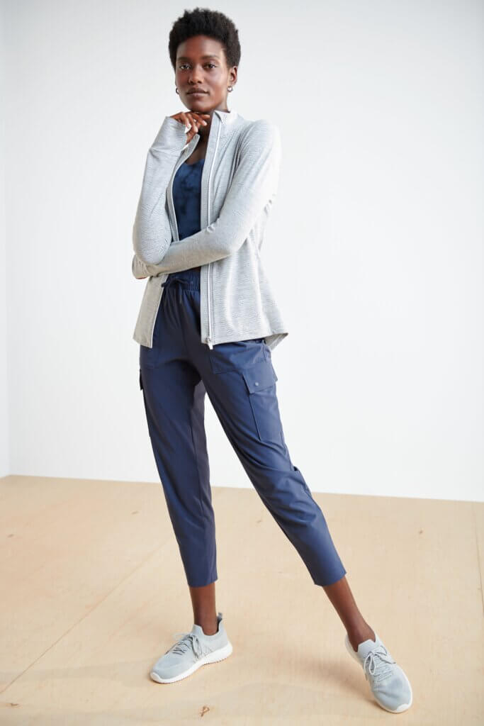 Stitch Fix model wearing women's golf attire outfit including navy shirt, navy cargo capris, grey jacket and sneakers.
