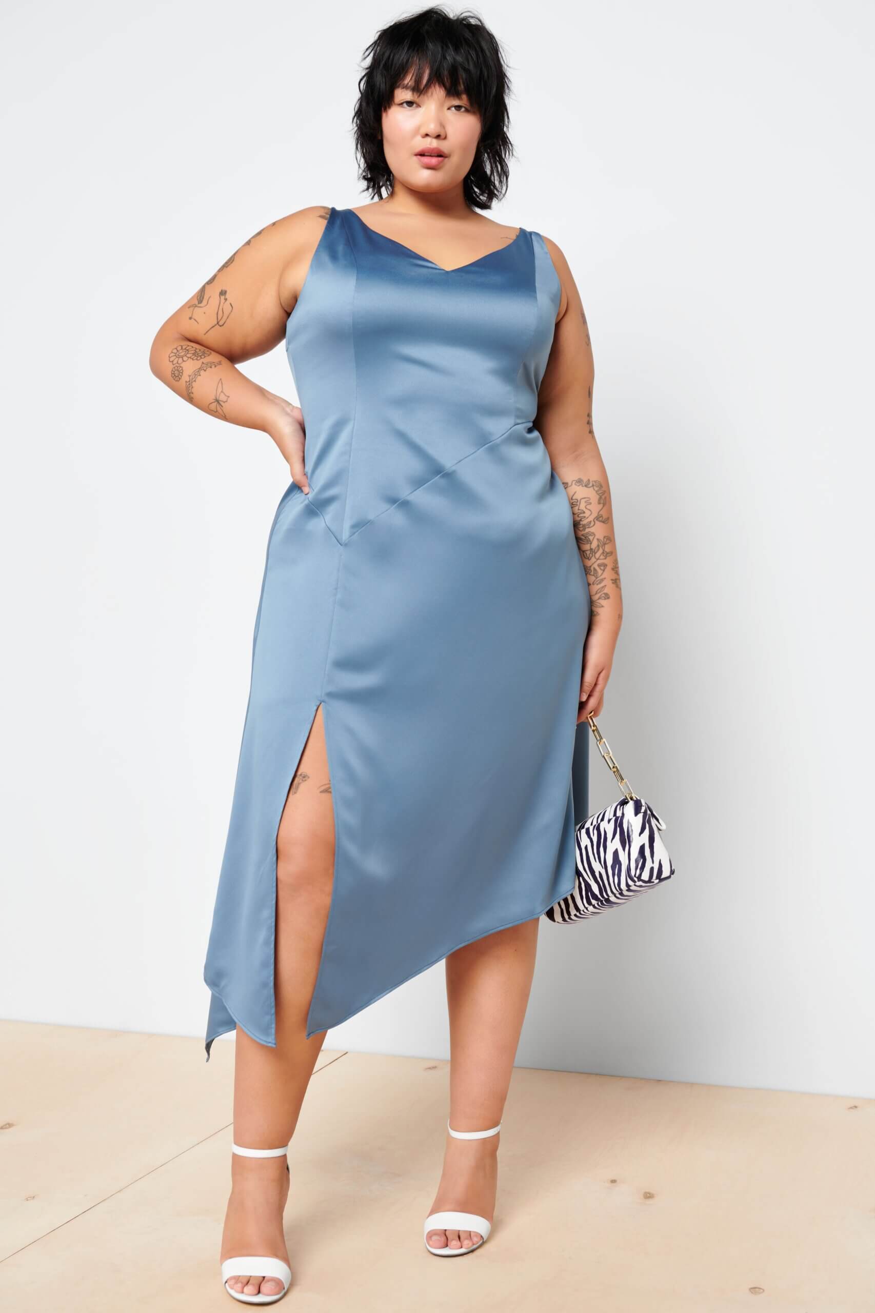 Stitch Fix women’s model wearing a sleeveless midi accessorized blue dress for a wedding with white heels and a zebra print purse.