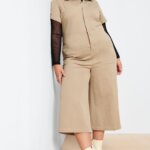 Stitch Fix model wearing women's 90s fashion outfit with black sheer shirt, tan cropped jumpsuit, purple beanie and white lug boots.