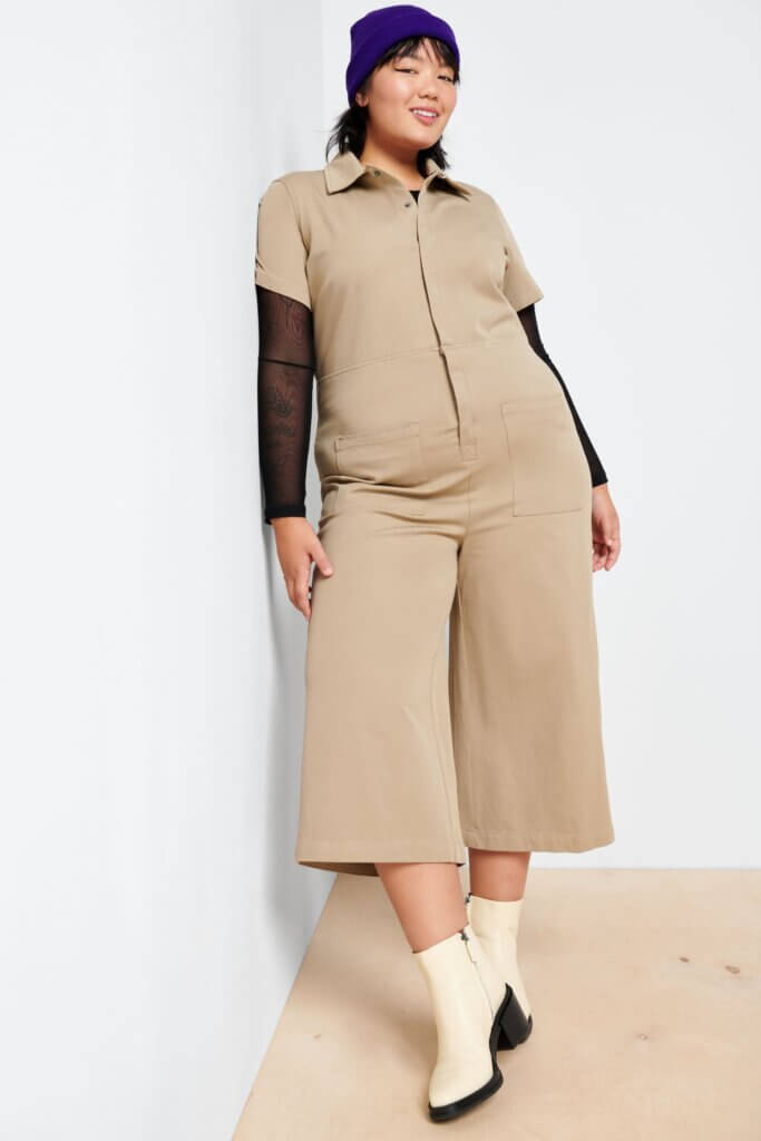 Stitch Fix model wearing women's 90s fashion outfit with black sheer shirt, tan cropped jumpsuit, purple beanie and white lug boots.