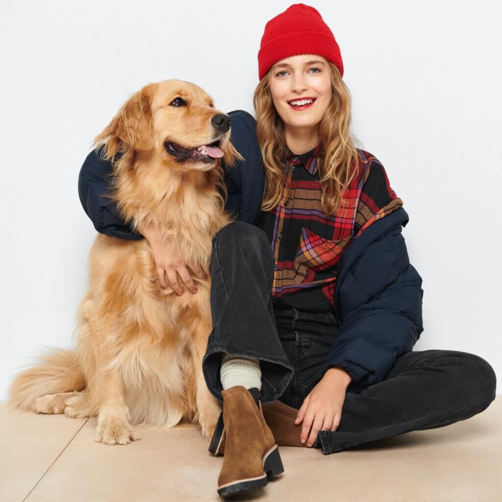 Stitch Fix model wearing women’s hiking outfit with beanie, plaid shirt, black jeans and boots next to golden retriever dog.