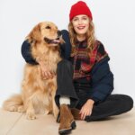 Stitch Fix model wearing women’s hiking outfit with beanie, plaid shirt, black jeans and boots next to golden retriever dog.