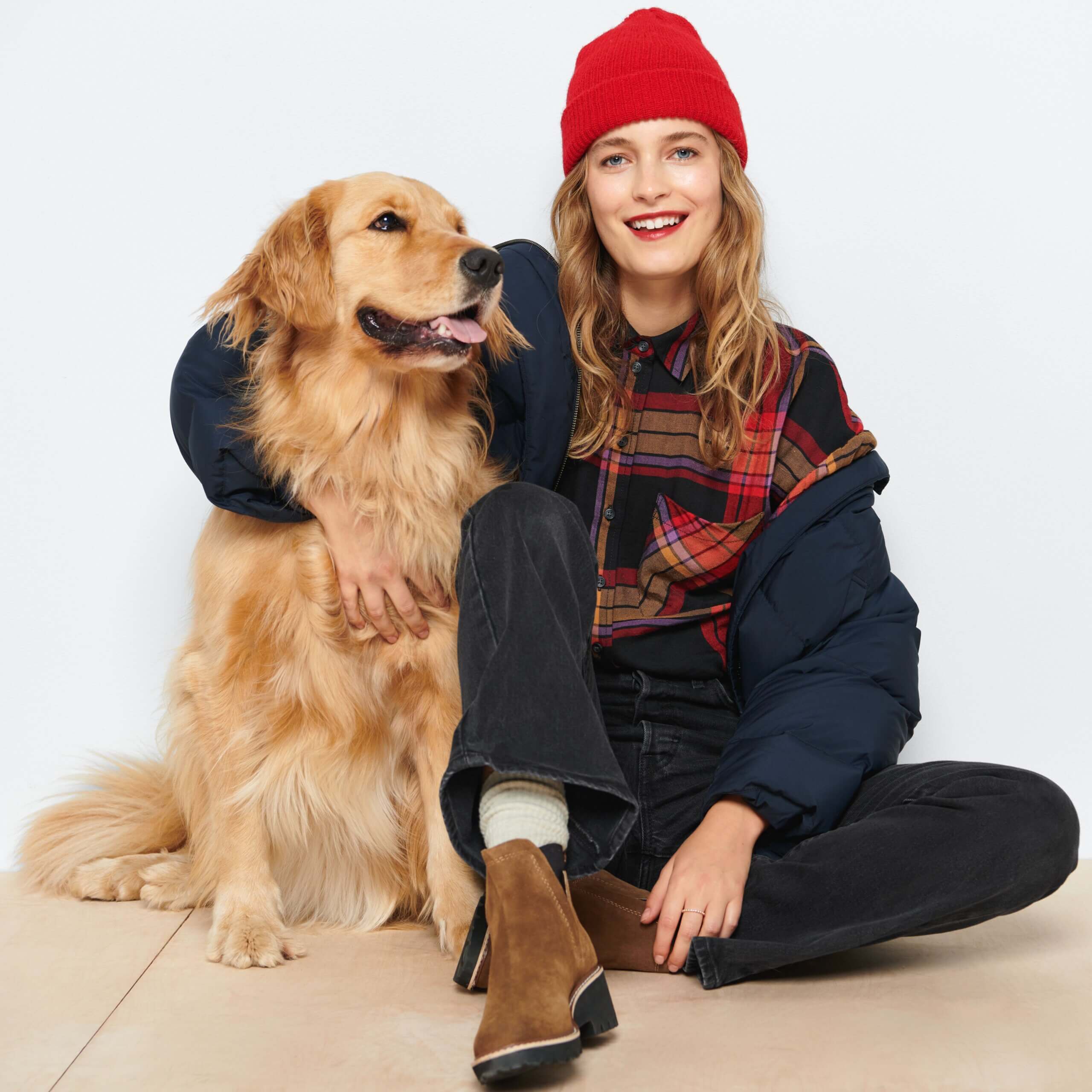 Stitch Fix model wearing women’s hiking outfit with beanie, plaid shirt, black jeans and boots next to golden retriever dog.