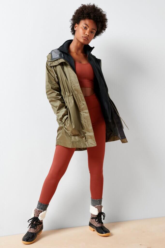 Stitch Fix model wearing women’s hiking outfit with burnt orange sports bra and leggings, hooded parka, socks and printed boots.