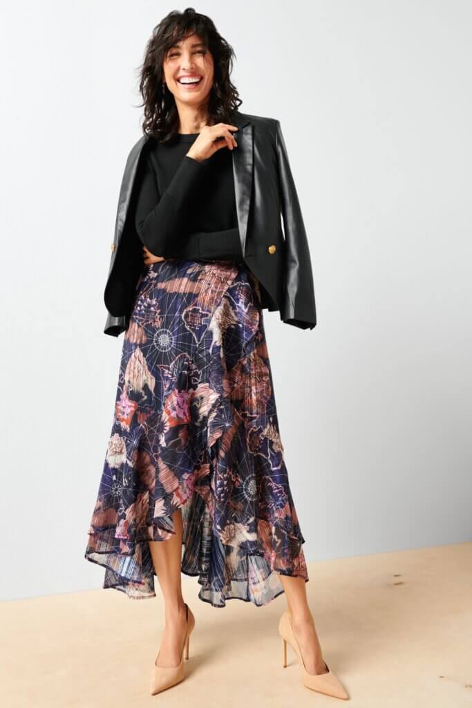 Stitch Fix model wearing printed wrap-over skirt outfit with a black crew neck sweater, black leather blazer and tan pumps.