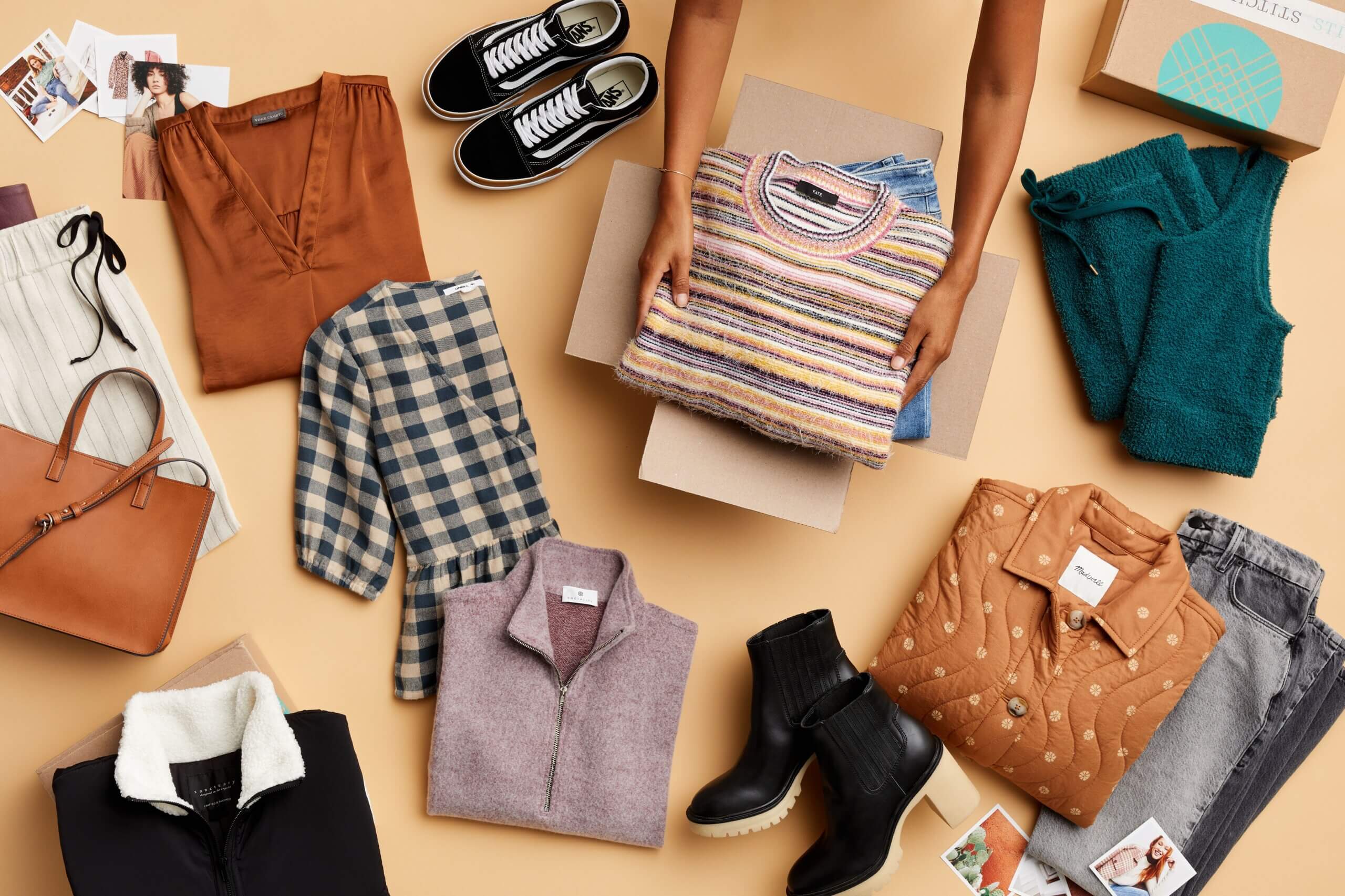 Stitch Fix women’s laydown featuring folded sweater and jeans in Stitch Fix delivery box next to black Vans sneakers, blouses in burnt orange and black plaid, cream pants, cognac tote, black sherpa pullover, purple knit top, black heeled booties, orange quilted jacket, faded blue jeans and green fuzzy lounge pants.