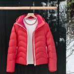 Stitch Fix women’s white shirt and red puffer jacket with hood on hanger in front of external wall with snow.