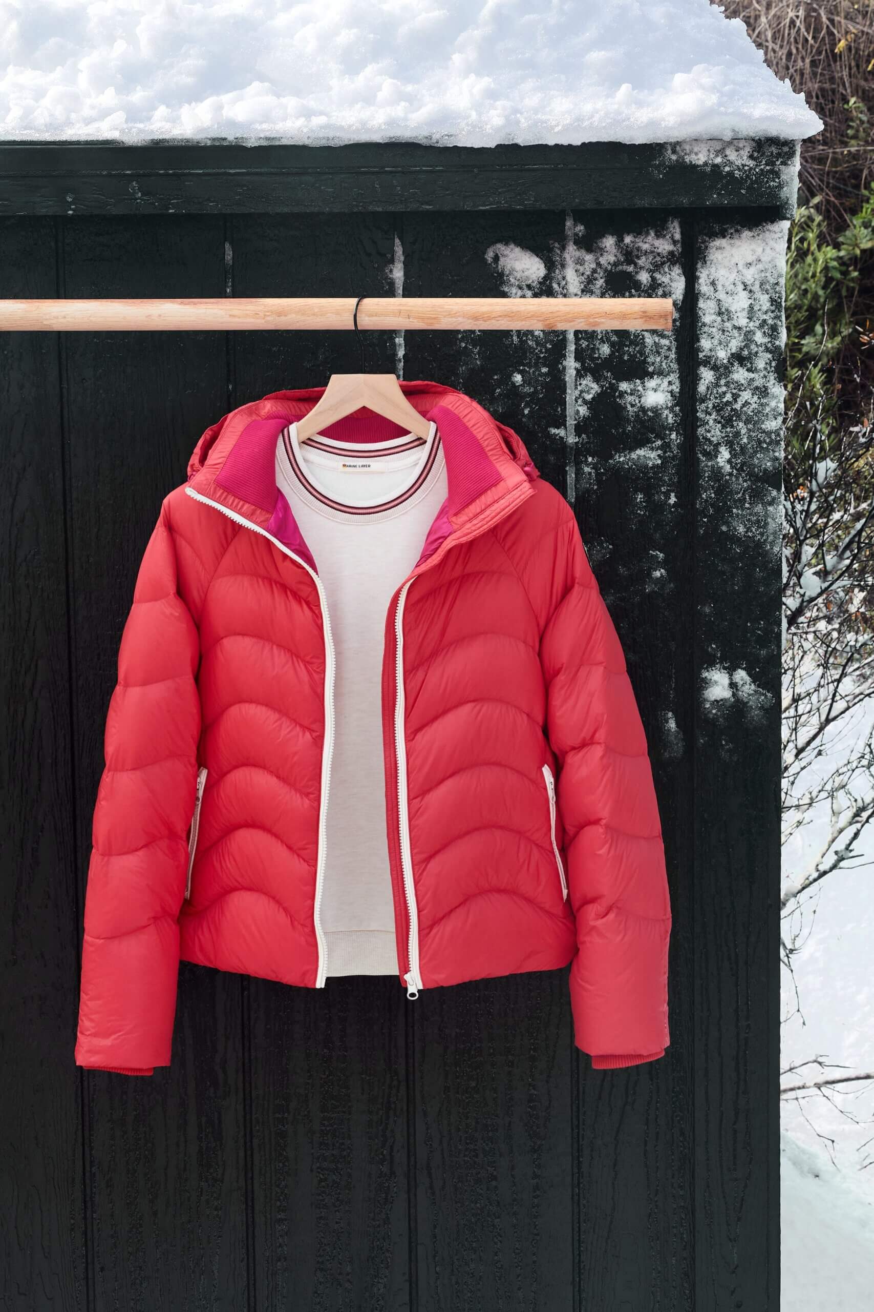 Stitch Fix women’s white shirt and red puffer jacket with hood on hanger in front of external wall with snow.