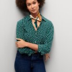 Stitch Fix model in French style outfit of teal printed button down, blue denim and a neck scarf.