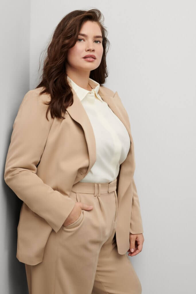Stitch Fix model wearing women’s business formal outfit with tan dress pants, matching blazer and white button-down shirt.