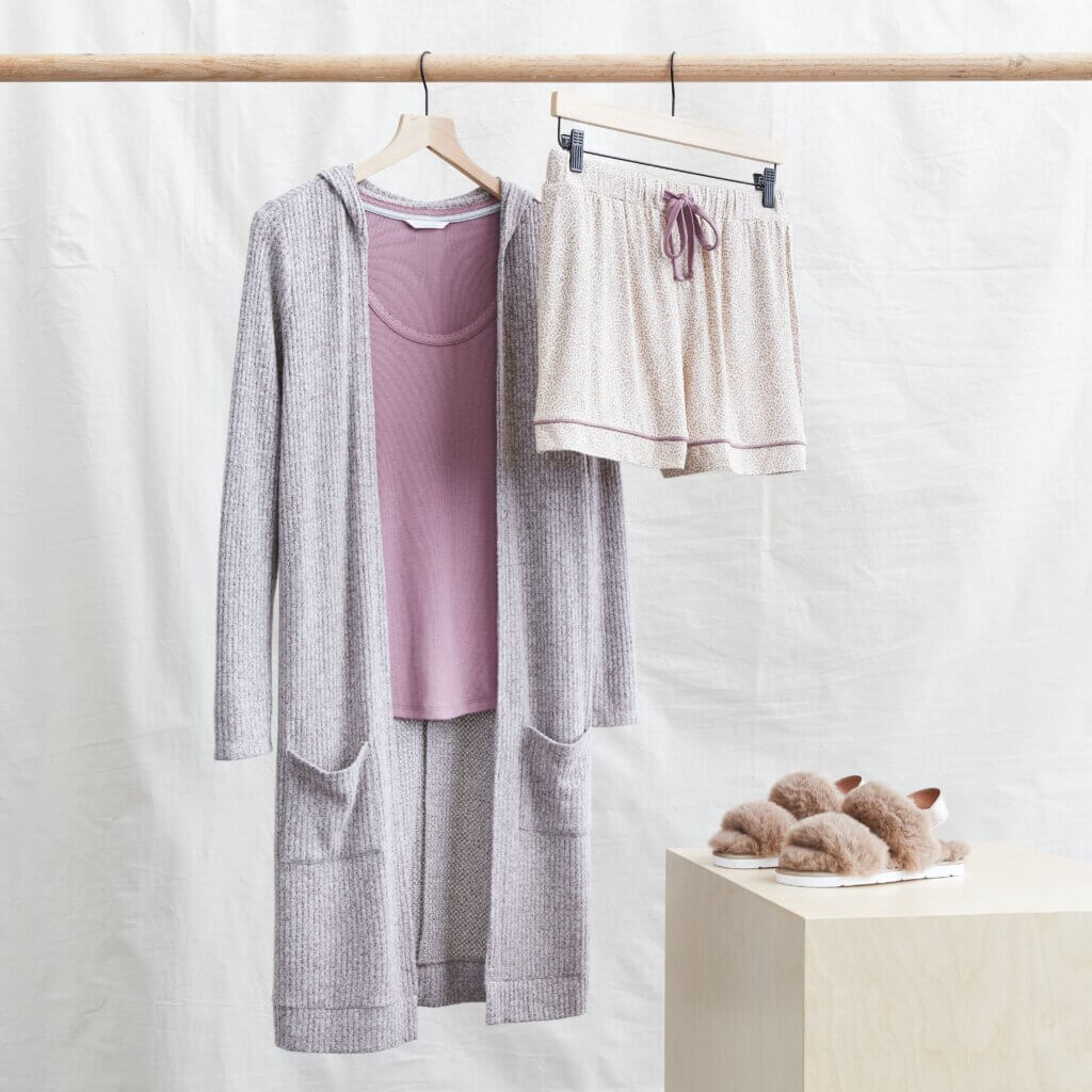 Stitch Fix women’s comfy road trip outfit with pink lounge shorts, pink top, duster cardigan hanging next to fuzzy slippers.