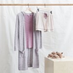 Stitch Fix women’s comfy road trip outfit with pink lounge shorts, pink top, duster cardigan hanging next to fuzzy slippers.