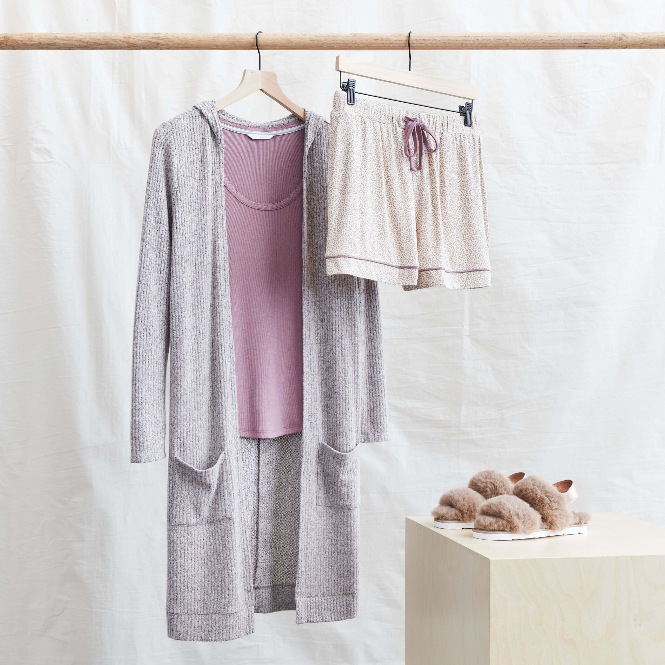 Stitch Fix women’s comfy road trip outfit with pink lounge shorts, pink top, duster cardigan hanging next to fuzzy slippers.