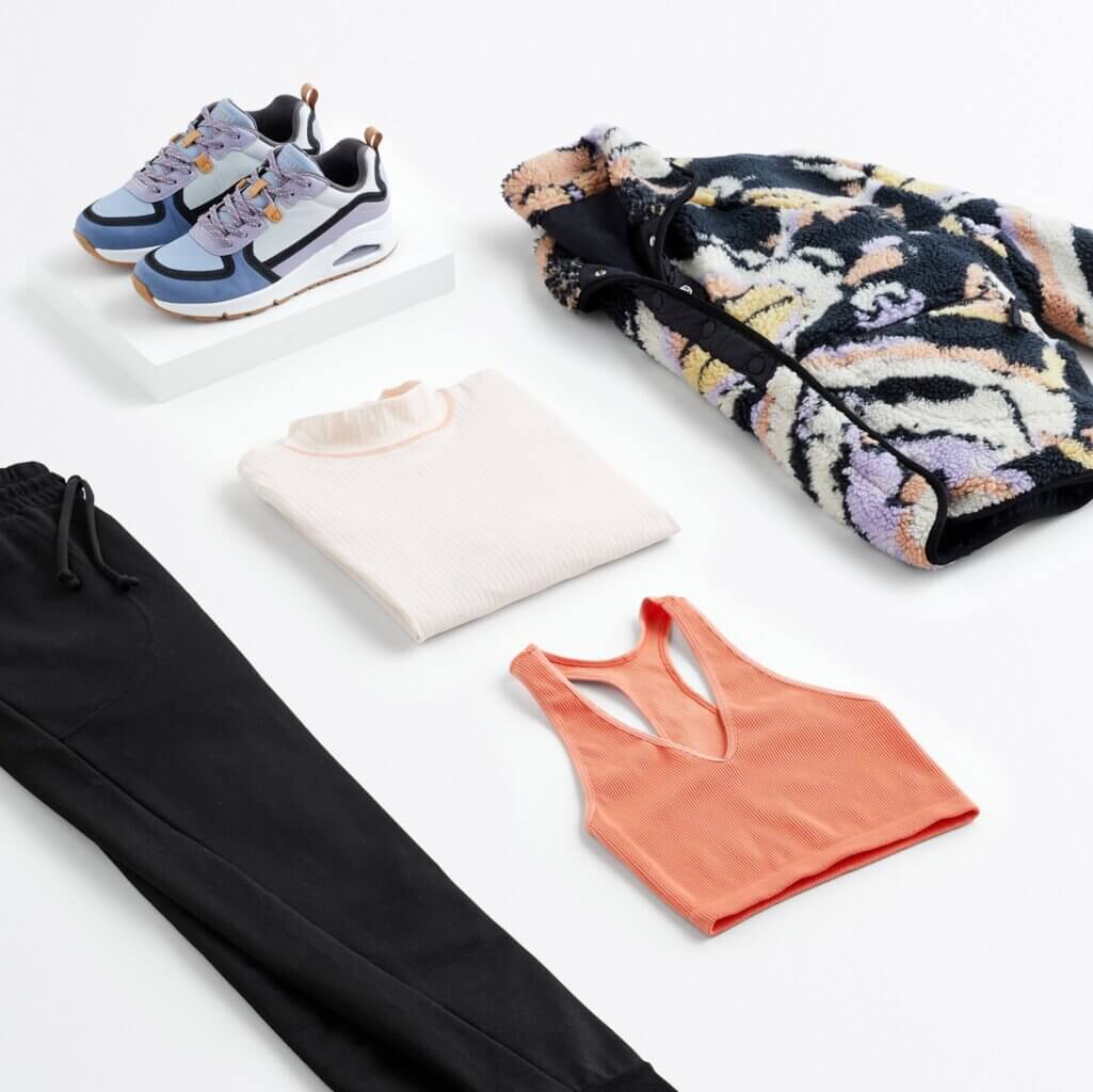 Stitch Fix women’s what to wear hiking outfit with black joggers, coral sports bra, white long-sleeve shirt, sneakers and graphic fleece jacket.