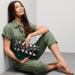 Stitch Fix model carrying women's black and white clutch with fringe wearing an olive jumpsuit, tan sandals and a printed scarf.