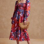 Stitch Fix model wearing women’s beach wedding guest attire with multicolor print midi dress, rattan clutch and orange heels.