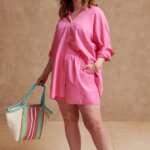 Stitch Fix model wearing women’s comfy road trip outfit with pink woven button-up shirt, shorts, colorful tote, woven hat and sandals.