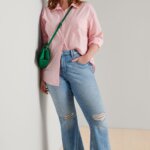 Stitch Fix model wearing women's 90s normcore fashion outfit with pink shirt, bootcut jeans, green bag and white sneakers and hat.
