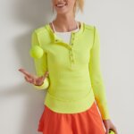 Stitch Fix women’s model wearing a tennis skirt outfit including an orange skirt, white halter tank and lime green long-sleeve henley.