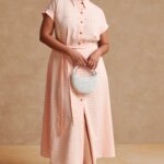 Stitch Fix model wearing women’s beach wedding guest attire with gingham dress, white handbag and brown braided heels.