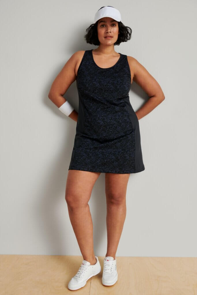 Stitch Fix women’s model wearing a tennis outfit including black active dress, white sneakers, wrist band and white visor.