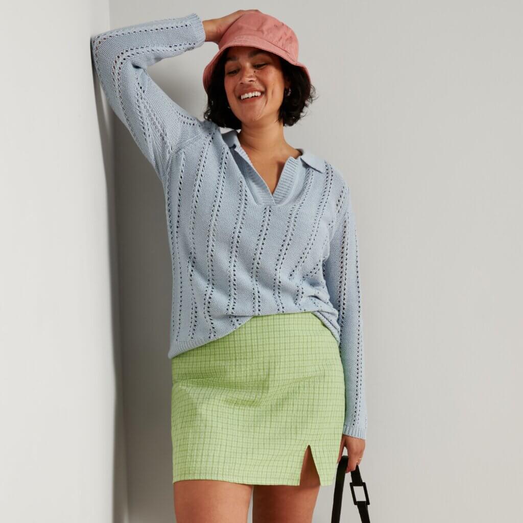 Stitch Fix model in women's Y2K fashion outfit with green mini skirt, blue collared sweater, bucket hat, purse and white sneakers.