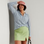 Stitch Fix model in women's Y2K fashion outfit with green mini skirt, blue collared sweater, bucket hat, purse and white sneakers.