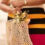Stitch Fix model carrying tan macrame type of bag, wearing a striped dress.