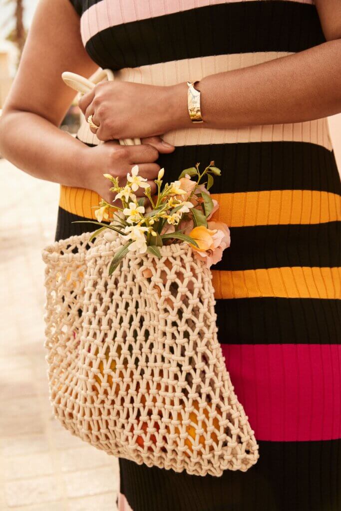 Stitch Fix model carrying tan macrame type of bag, wearing a striped dress.