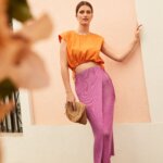 Stitch Fix model wearing women’s beach chic wedding attire with orange cropped top, fuchsia wrap skirt, sandals and clutch.