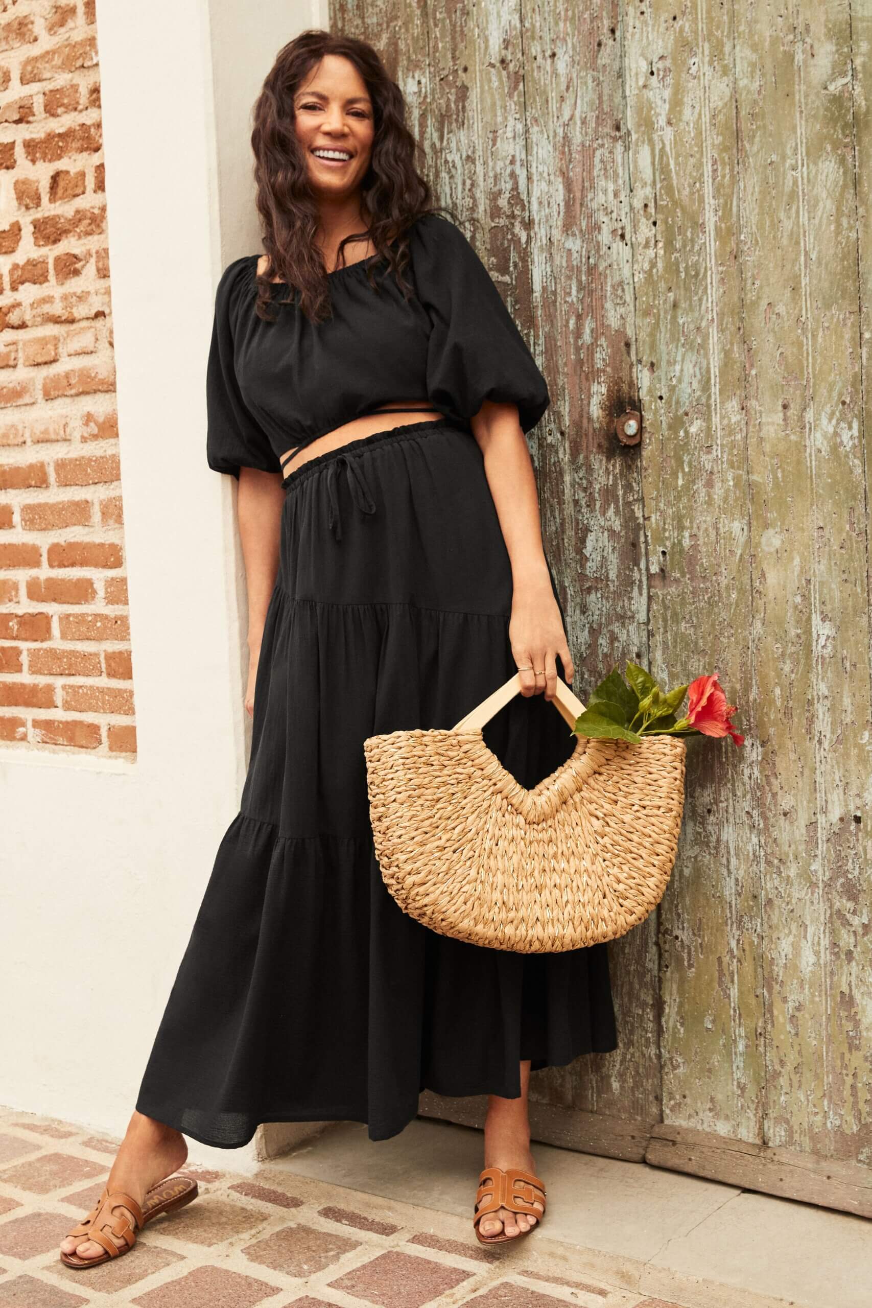 Stitch Fix model wearing women’s coastal grandmother outfit with black crop top, maxi skirt and straw purse with flower.