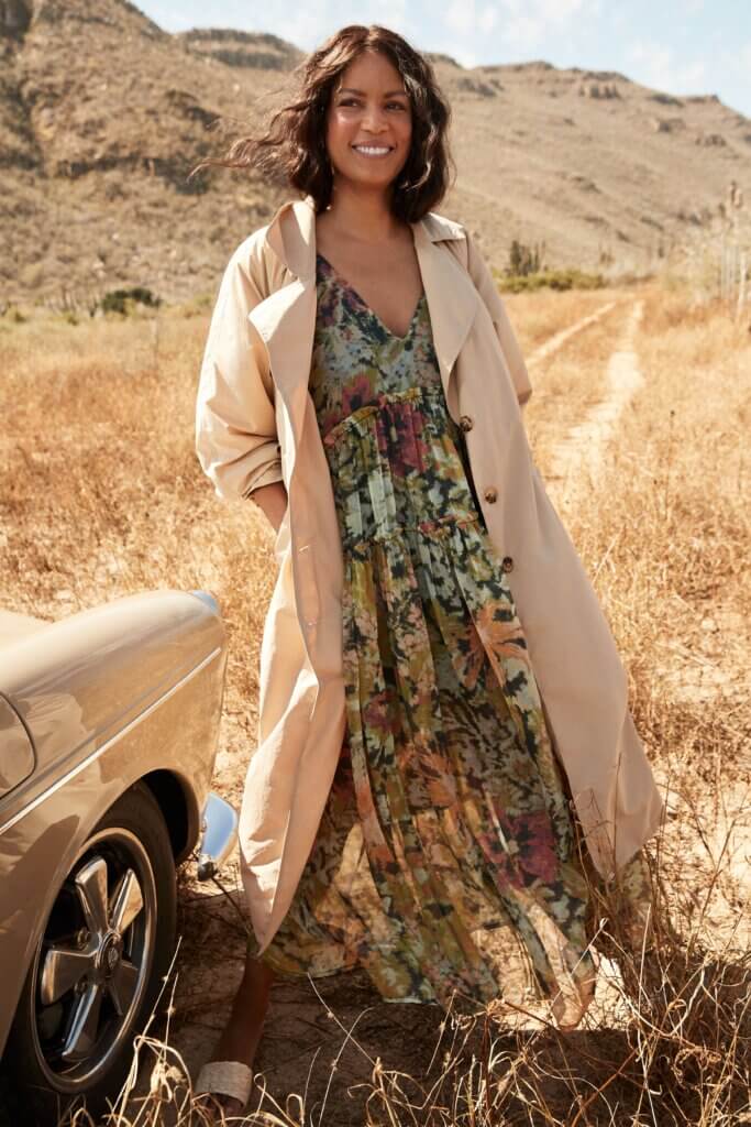 Stitch Fix model wearing women’s casual beach wedding attire with multicolor floral maxi dress and tan trench jacket.