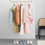 Stitch Fix Bridgerton-inspired women’s clothing featuring blue blouse, green dress, tan blazer, ivory pants and blush tie waistcoat on hangers with assorted shoes.