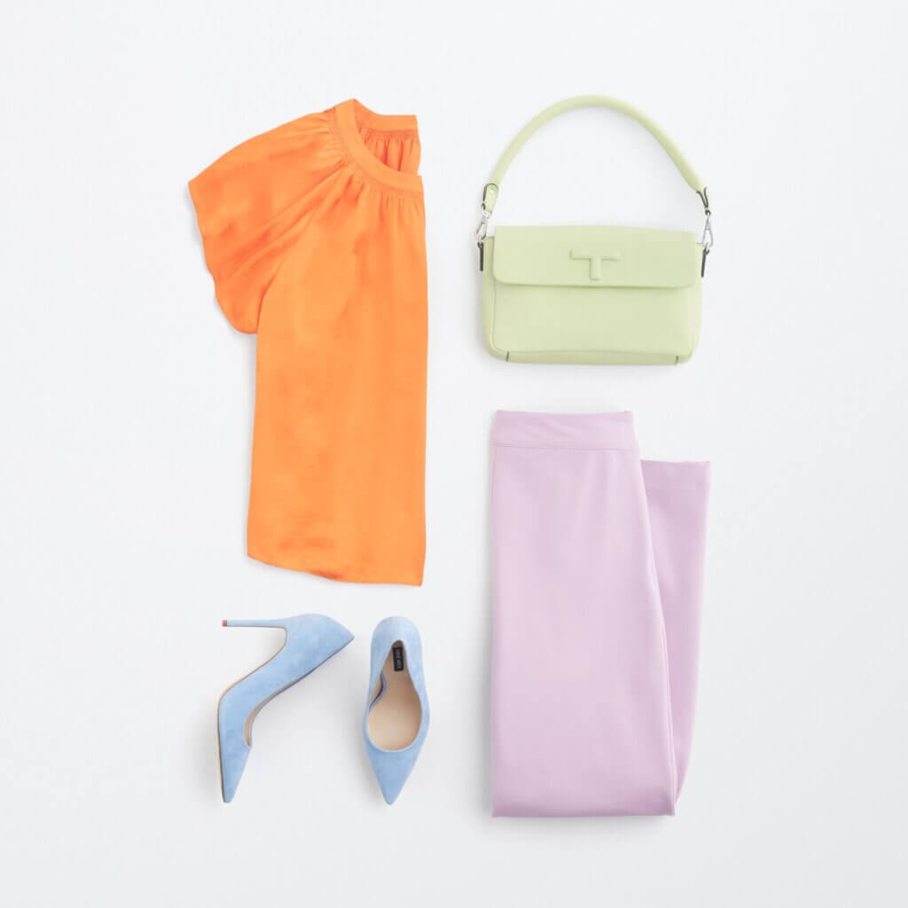 Stitch Fix women's semi-formal wedding attire outfit with orange short-sleeve top, lavender pants, blue pumps and light green bag.